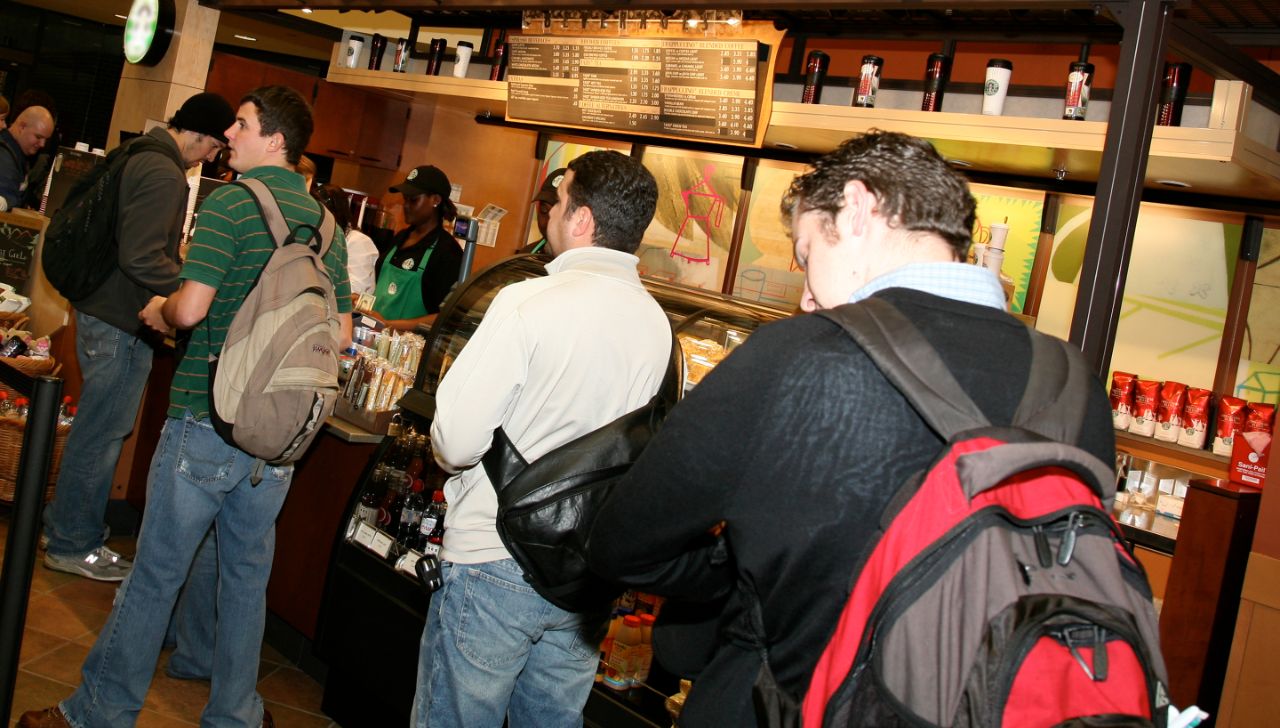 Four male students standing in line at Starbucks for coffee.