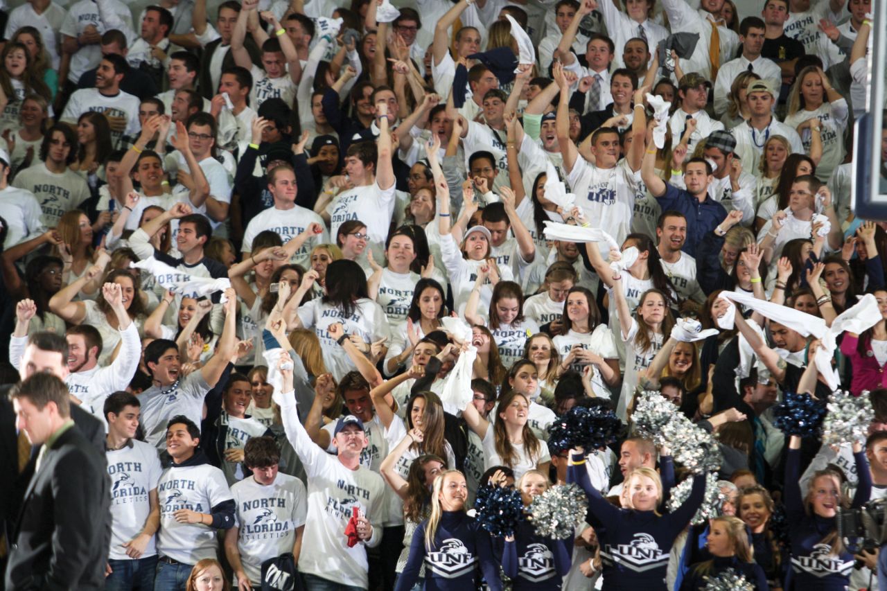 A large group of people cheering at a basketball game.