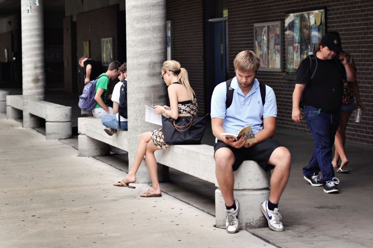 Students sitting on concrete benches reading and a few students walk by.