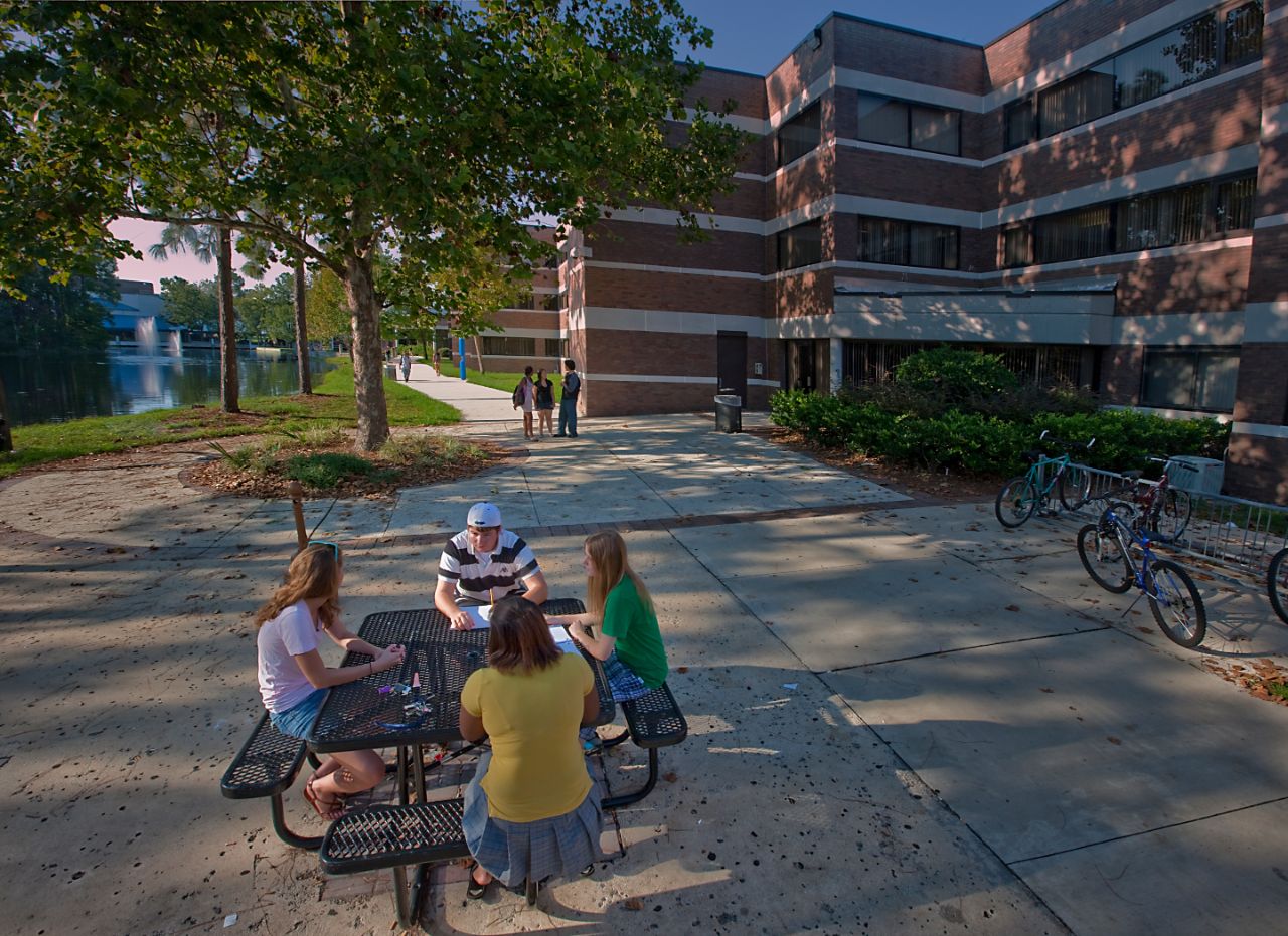 Three females and a male side around a picnic table talking.