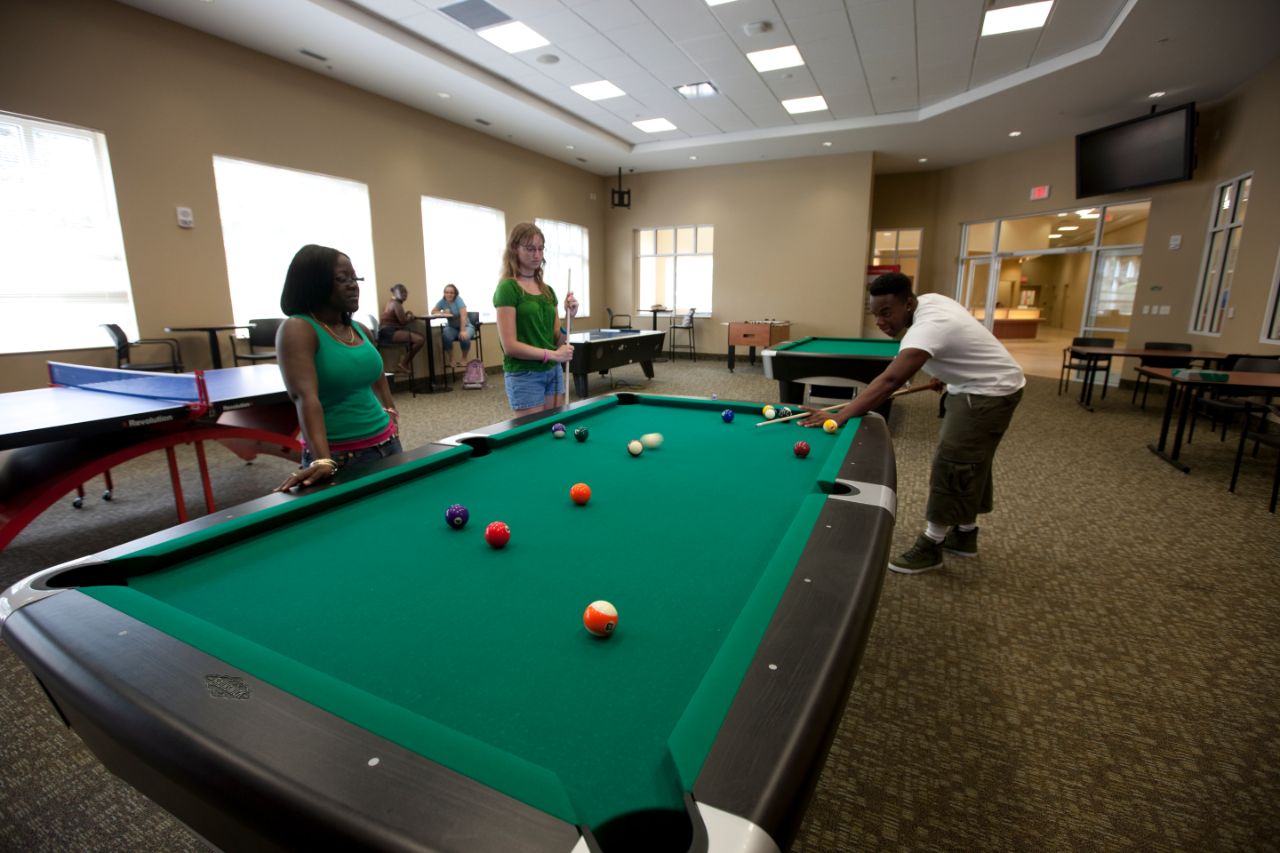 Two females and one male around a billiard table. The male is leaning down to make a shot.