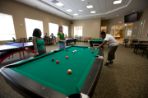 Two females and one male around a billiard table. The male is leaning down to make a shot.