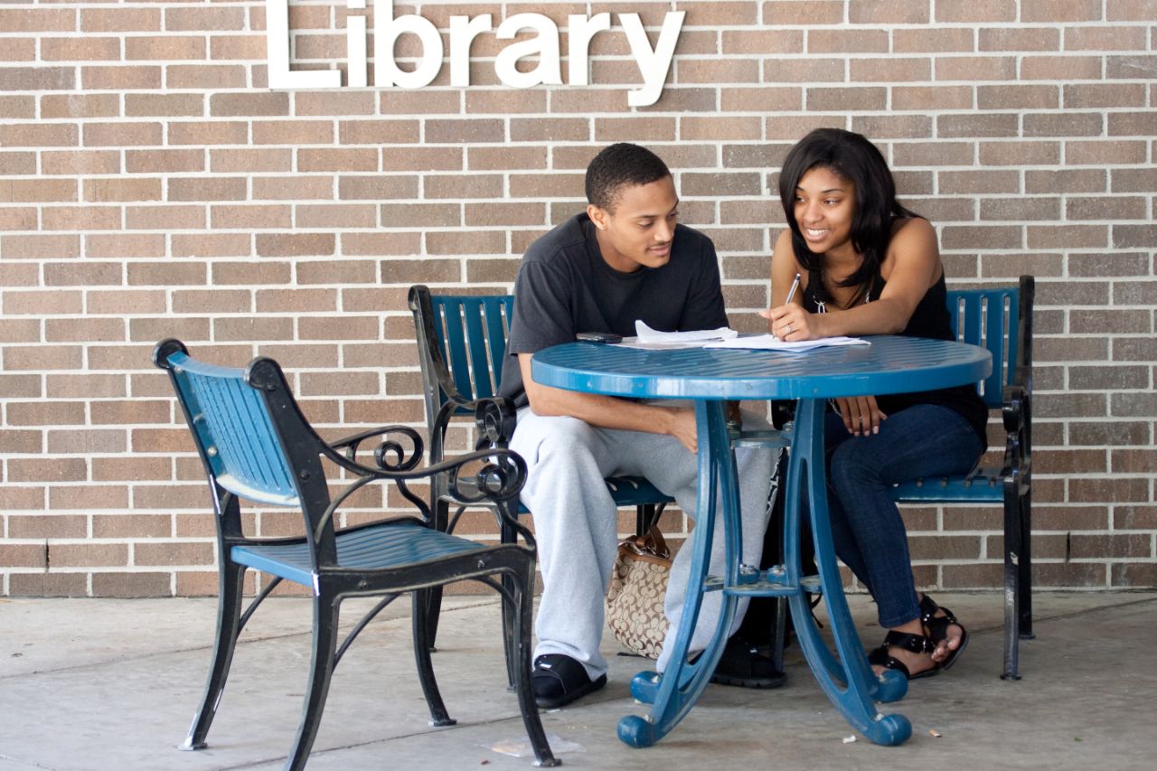 A male and female student sitting at a round table studying in front of the Library.