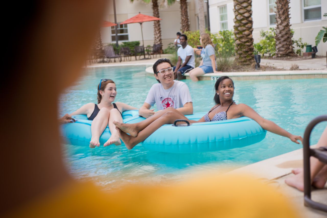 Two females on floats with a male standing in the water behind them in the pool.