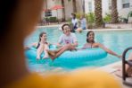 Two females on floats with a male standing in the water behind them in the pool.