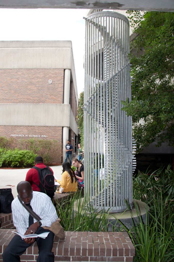 Two males and two females sit on a brick wall outside of Schultz Hall studying.