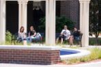 Three female students and one male student sit on benches at the Meditation Pond in front of the Brooks College of Health.