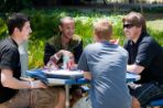 Four males sitting around a picnic table eating and talking.