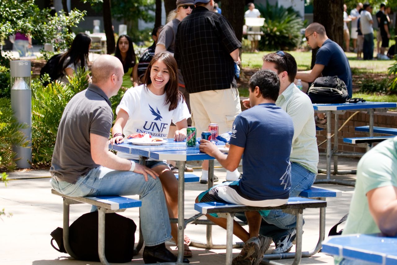 Three male students and one female student sit around a picnic table eating lunch.