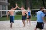 Two males high-fiving on a volleyball sand court.