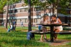 Two females sit at a picnic table studying. Students in the background on a swing.