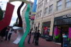 Three male students stand between the front door of the Museum of Contemporary Arts and a large colorful sculpture on the sidewalk.