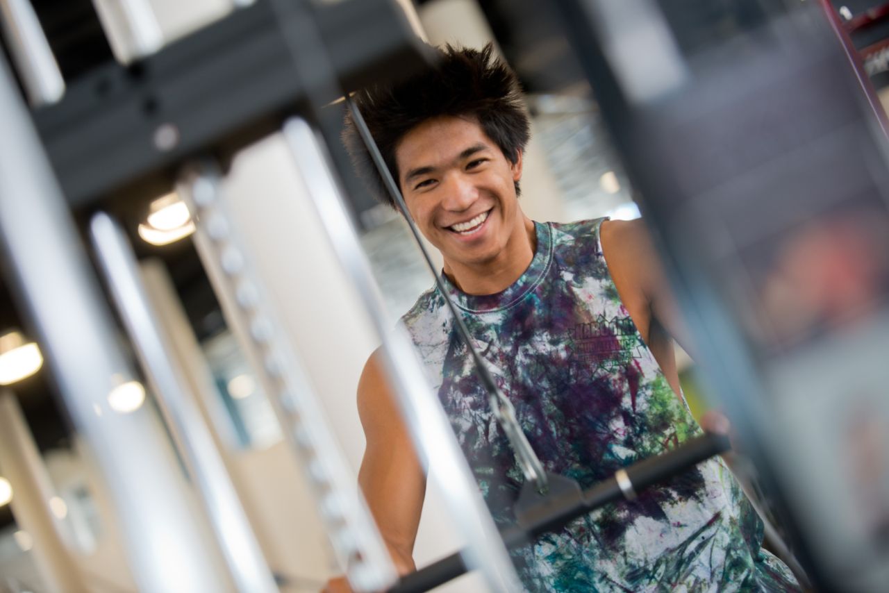 A male smiling as he works out on a weight machine.