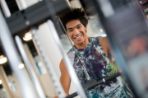 A male smiling as he works out on a weight machine.