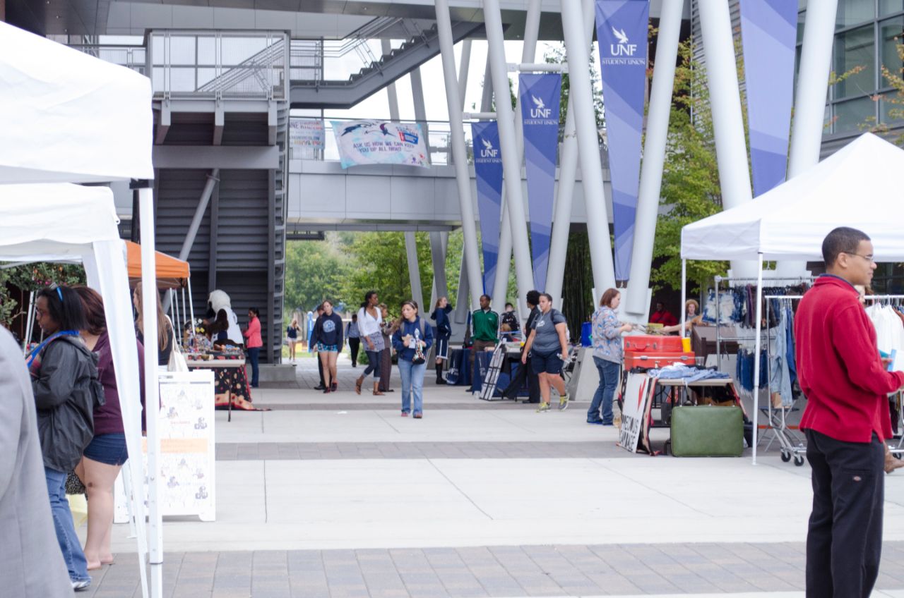 Several tables set up in the plaza with people walking to the booths.