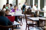 A lot of tables with the focus of a female working on her laptop.